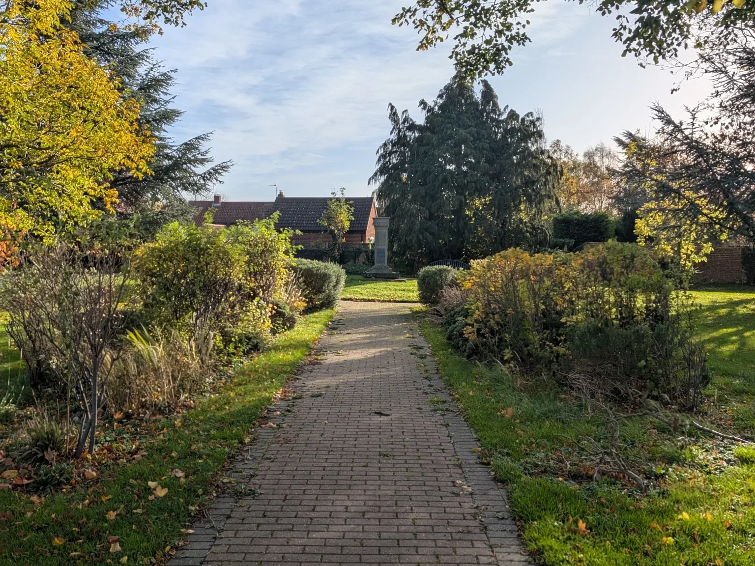 A picture of a war memorial at the end of a path in a small park.
